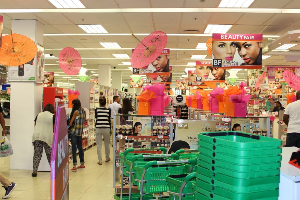 Loja de cosméticos com cestinhas e carrinhos, várias prateleiras com produtos e pessoas comprando.